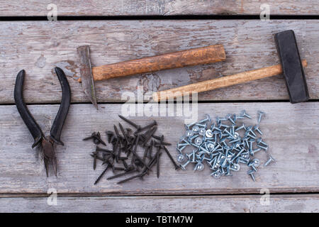 Strumenti di costruzione su sfondo di legno. Due antichi magli, pinze e molte viti su rustiche tavole di legno. Concetto di riparazione. Foto Stock