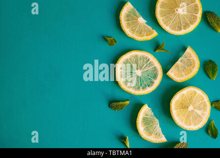 Le fette di limone e menta erbe contro blu sullo sfondo a trama con copyspace. Vista dall'alto di limoni e foglie Foto Stock