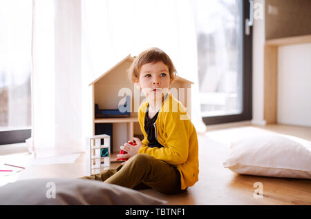 Una piccola ragazza che gioca con la casa di legno sul pavimento a casa. Foto Stock