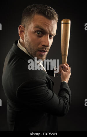 Imprenditore o un uomo in abito formale su sfondo scuro. Uomo sulla faccia di rigorosa in posa con la mazza di legno. Uomo con setola guarda fiducioso e minaccioso. Aggressivo il concetto di business. Foto Stock