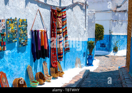 Blu e bianco tradizionale street nella Medina di Rabat. Sulla parete appendere i tappeti e i magneti per la vendita in Marocco Foto Stock