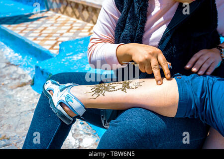 Artista applicando henna tattoo sulla gamba di donne per le strade di Marrakech in Marocco Foto Stock