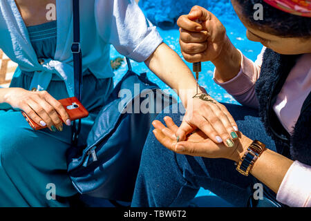 Artista applicando henna tattoo sulle mani delle donne nelle strade di Marrakech in Marocco Foto Stock