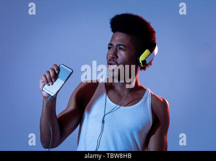 Forte americano africano giovane uomo ascoltare musica online in app per smartphone per ballare e cantare con le cuffie. Close up ritratto con discoteca dance Foto Stock