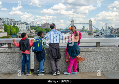 Una famiglia asiatica visitare Londra e prendere un selfie con il fiume Tamigi e il Tower Bridge in background. Foto Stock