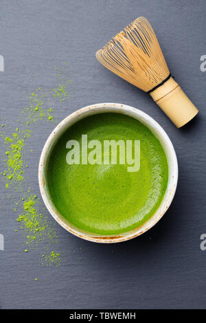 Tè verde Matcha il processo di cottura in una ciotola con una frusta di bambù. Nero ardesia sfondo. Vista dall'alto. Foto Stock