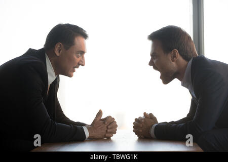 Mad imprenditori yell seduto in confronto a tavola Foto Stock