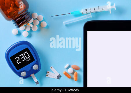 Close up vista dall'alto in basso del glucometro, farmaco pillole, siringa da insulina e tablet pc con una schermata bianca vuota per copia spazio su sfondo blu. Il diabete Foto Stock