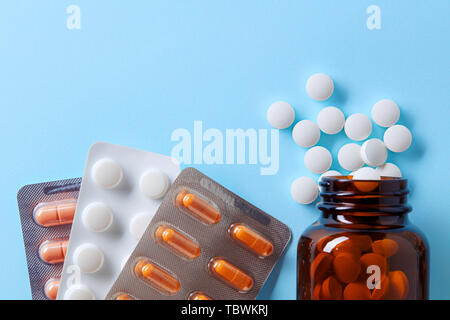 Medico farmaceutica pillole, capsule in blister e compresse si versato da un flacone di farmaco su sfondo blu Foto Stock