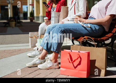 Close-up di un irriconoscibile ragazza shopper in abiti casual seduta sul banco di prova all'aperto e di bere il caffè durante il riposo dopo lo shopping Foto Stock