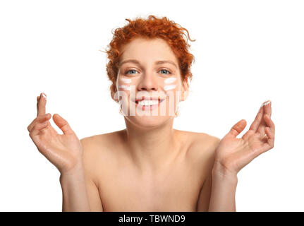Bella redhead donna l'applicazione di crema per il viso contro uno sfondo bianco Foto Stock
