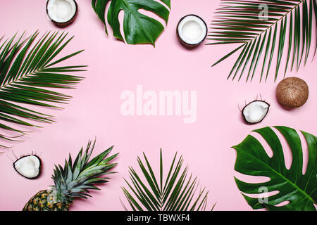 Ananas maturi, noci di cocco, noci tropicali e palme verdi foglie di monstera su sfondo rosa con spazio per il testo. Layout creativi. Concetto di estate. Piatto, laici t Foto Stock