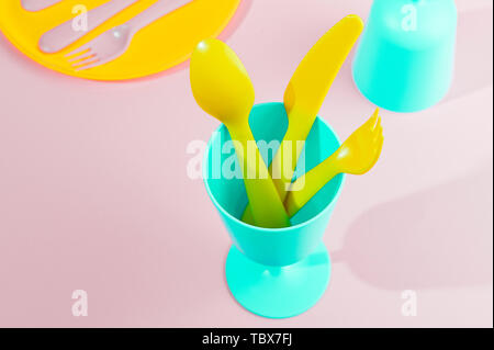 Colore luminoso picnic in plastica utensili. Rosa, giallo, blu nel recipiente. Foto in hard light. Spazio di copia Foto Stock