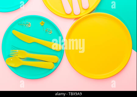 Colore luminoso picnic in plastica utensili. Rosa, giallo, blu nel recipiente. Foto in hard light. Copia dello spazio. Foto Stock