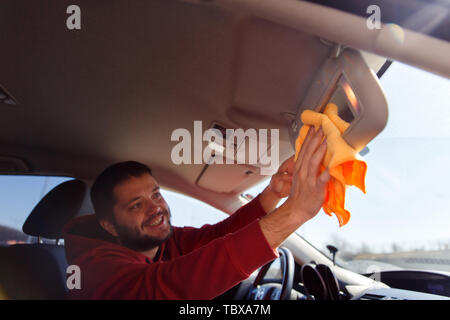 Foto a lato del felice maschio con orange rag specchio di lavaggio della macchina Foto Stock