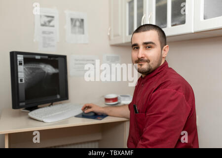 Un medico radiologo sul posto di lavoro guarda le immagini da una macchina a raggi X sul monitor di un computer. Foto Stock