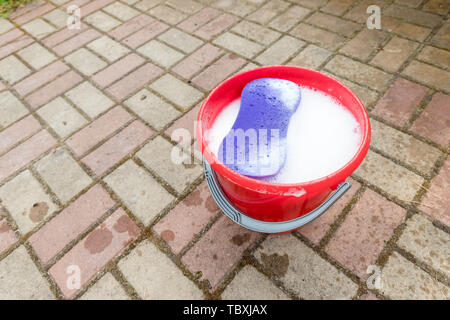 Un rosso secchio di plastica su ciottoli con sfondo di colore viola spugna. Tema di pulizia.apparecchi per uso domestico a casa di fondo interna, la molla Foto Stock