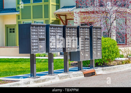 Fila di cassette postali di cluster con scomparti numerati su un marciapiede soleggiato Foto Stock