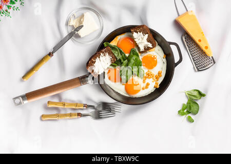 Padella con uova fritte su uno sfondo luminoso. tovaglia bianca, piatto laici. Foto Stock