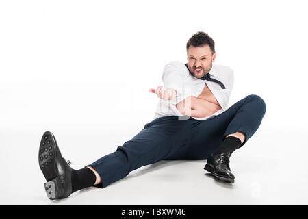 Adirato contro il sovrappeso uomo in stretto usura formale gesticolando con la mano mentre è seduto su bianco Foto Stock