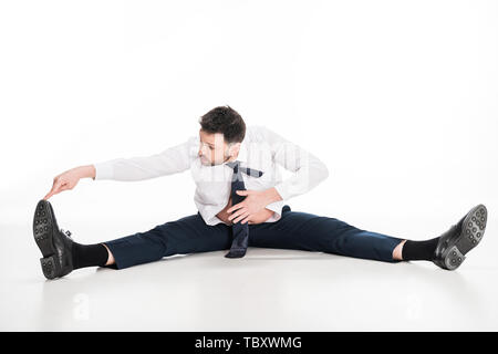 Il sovrappeso uomo in stretto formale seduta di usura e stretching su bianco Foto Stock