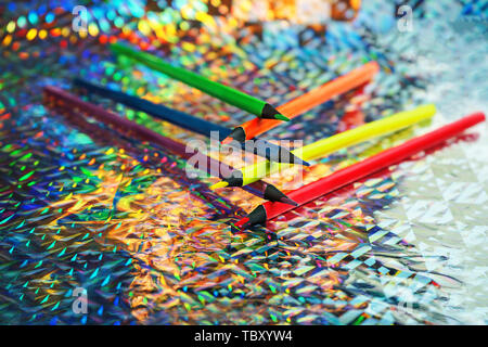 Si torna a scuola lo sfondo con luci al neon colorate matite a colori sulla lamina olografica sullo sfondo. Foto Stock