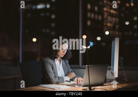 Giovane imprenditrice in linea di lavoro in un ufficio di notte Foto Stock