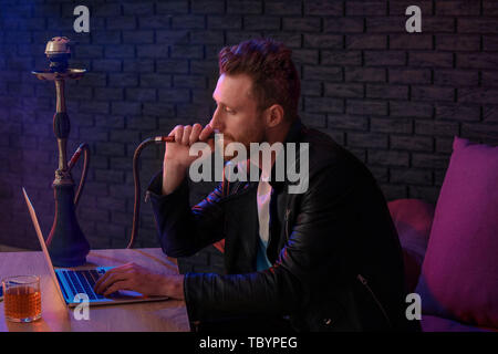 Giovane uomo di fumare narghilè mentre si lavora sul computer portatile in  cafe Foto stock - Alamy