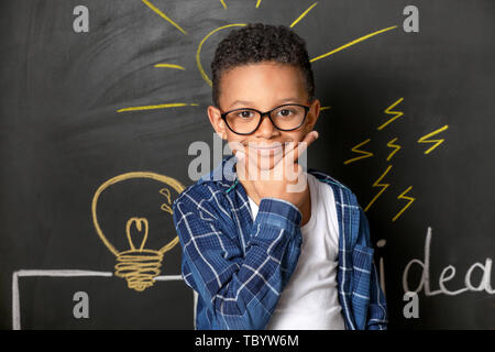 Premuroso ragazzo afro-americano vicino disegnato lampadina della luce sulla parete scura Foto Stock