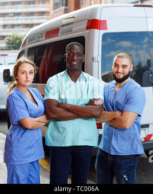 Ritratto di positivo sorridendo Gentile team di ambulanza di tre piedi vicino ambulanza Foto Stock