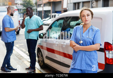 Ritratto di positivo efficiente ambulanza amichevole personale paramedico in piedi vicino a ambulanza Foto Stock