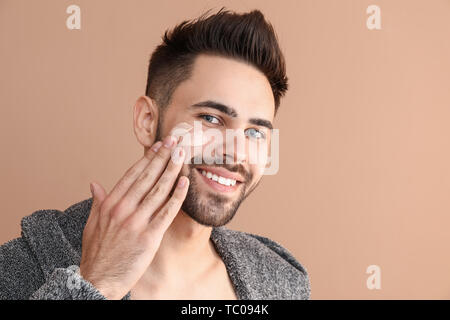 Uomo bello applicare la maschera di argilla sul suo volto contro il colore di sfondo Foto Stock