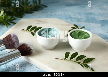 Ciotole con argille cosmetiche e spazzole sul colore di sfondo Foto Stock