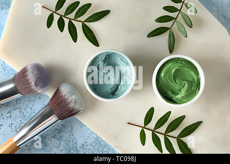 Ciotole con argille cosmetiche e spazzole sul colore di sfondo Foto Stock
