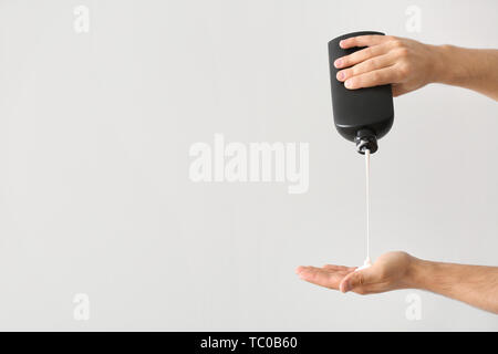 Mani maschio con bottiglia di shampoo su sfondo chiaro Foto Stock