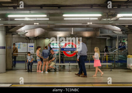 Persone sedersi su un banco di lavoro sulla piattaforma a Westminster Londra Stazione della Metropolitana Foto Stock