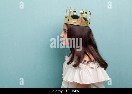 Vista laterale ritratto di grave adolescente bella bruna ragazza indossare Golden crown simbolo della principessa in abito bianco in piedi e guardando lontano. Indoor, Foto Stock