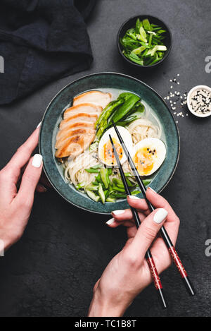 Pollo Ramen noodle soup nella ciotola. Mani tenendo le bacchette sulla ciotola del pasto asiatico. Sfondo nero Foto Stock