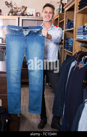 Cliente maschio esaminando i pantaloni in panni maschio store Foto Stock