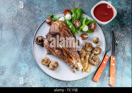 Agnello al forno con funghi, erbe e spezie su un piatto rotondo su un sfondo di calcestruzzo. La carne halal e cibo. Vista superiore Foto Stock