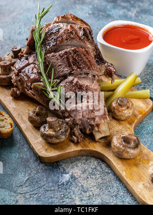 Close-up ram alla griglia della gamba con funghi, verdure, spezie su un tagliere. La carne halal e cibo Foto Stock