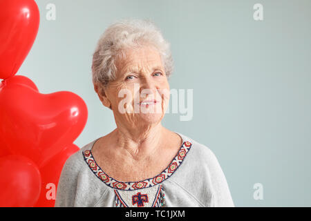 Ritratto di donna senior con a forma di cuore palloncini aria su sfondo grigio Foto Stock