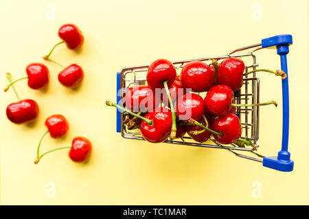 Mini carrello carrello del negozio pieno di ciliegie fresche. Frutti di bosco freschi su sfondo giallo. Un sano, estate food concept. Foto Stock