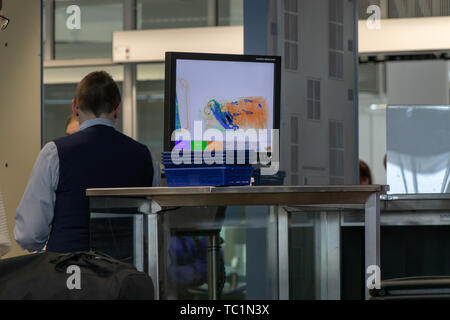 Aeroporto di Monaco di Baviera, 2019 aprile 09: un uomo in uniforme permanente al contatore al punto di controllo e guardare al monitor con raggi x del bagaglio. Foto Stock