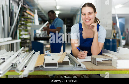 Ritratto di giovane donna capitano che sta lavorando con finestre moderne in officina. Foto Stock