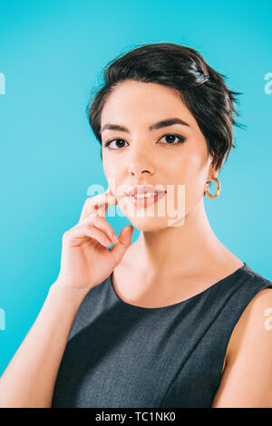 Ritratto di splendida razza mista donna che guarda la telecamera tenendo la mano vicino alla faccia isolato su blu Foto Stock