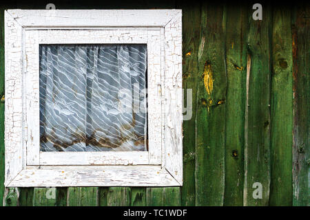 Piccola finestra quadrata sulla plancia verde parete ricoperta con tenda sporca. Architettura di sfondo di dettaglio Foto Stock