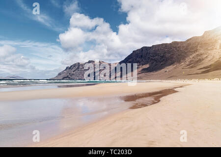 Ampia di sabbia spiaggia di Famara a Lanzarote, Spagna contro oceano Atlantico, montagne scoscese e bellissimo cielo Foto Stock
