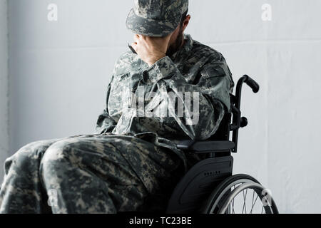 Premuto disabili uomo militare in uniforme seduto nella sedia a rotelle e che ricopre la faccia con la mano Foto Stock