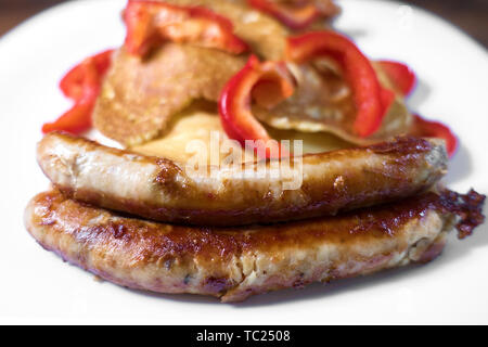 Salsicce fritte frittelle e pepe rosso giacciono su una piastra bianca in legno per lo sfondo. Foto Stock